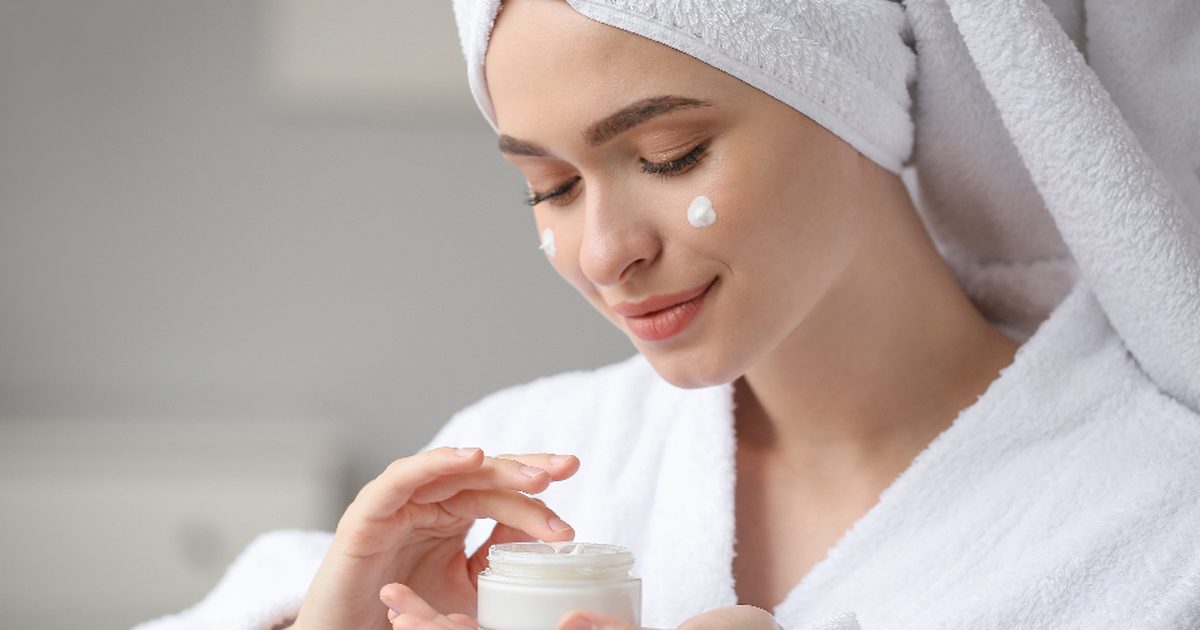 A woman in a towel applying a small amount of cream