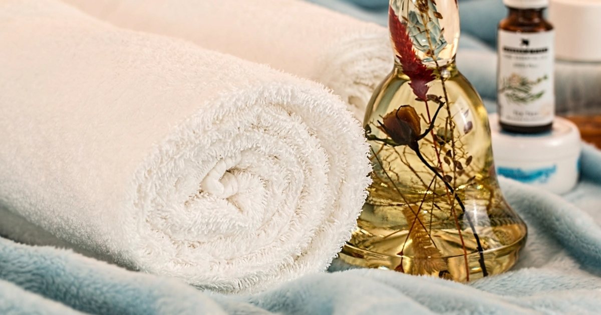 A rolled white towel beside a glass bottle of oil
