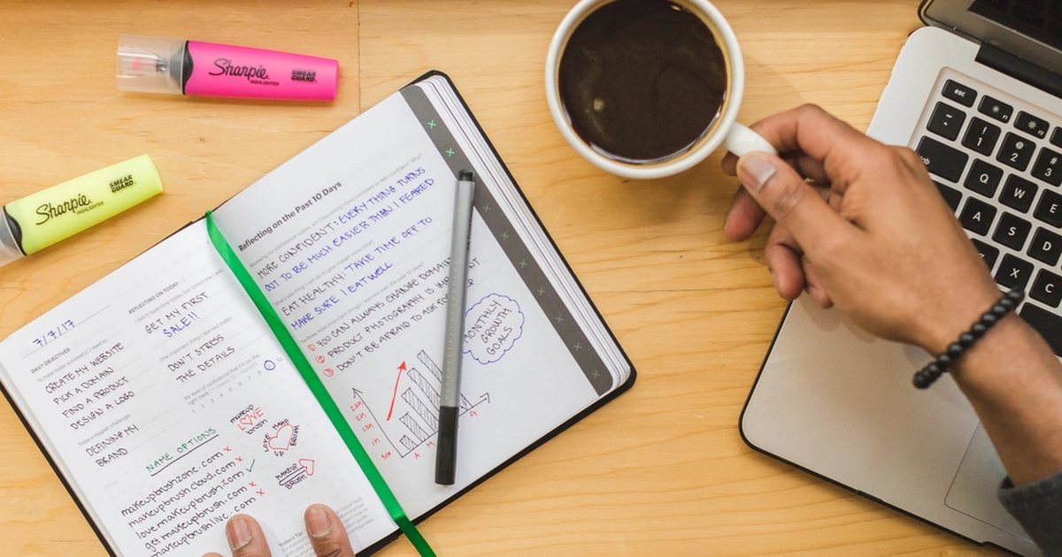 An open notebook with a pen and a cup of coffee on a desk