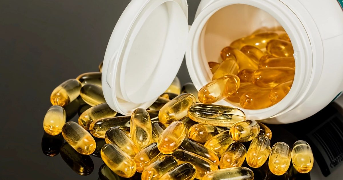 Golden softgel capsules spilling out of a white bottle